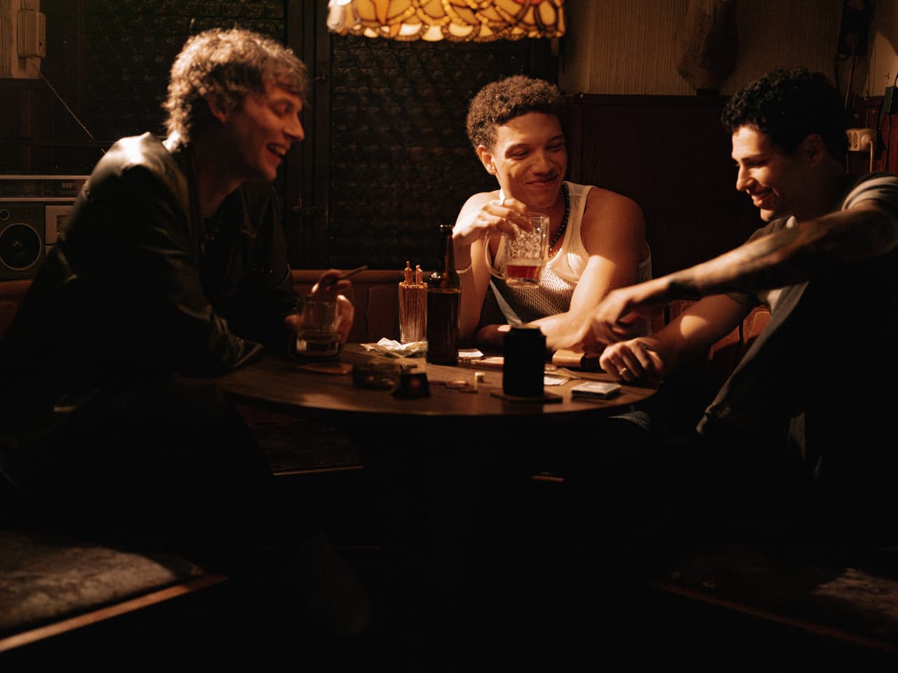 Three people around a small table in a dim bar, mid conversation